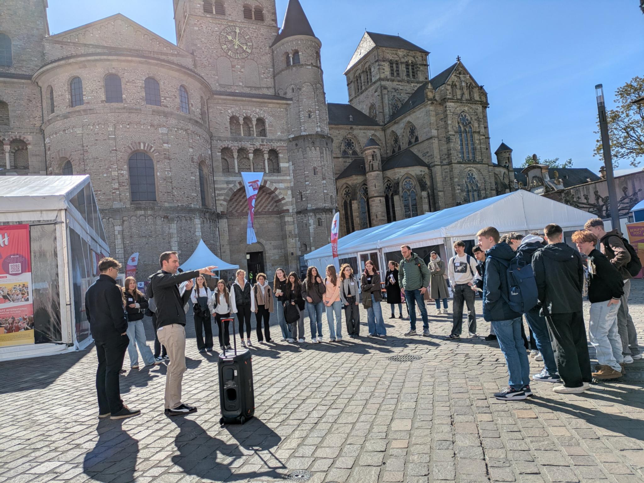 Eine Gruppe Jugendliche hört einem Moderator auf dem Domfreihof zu.