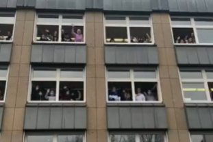 Viele Schüler*innen winken aus offenen Fenstern des Schulgebäudes in die Kamera