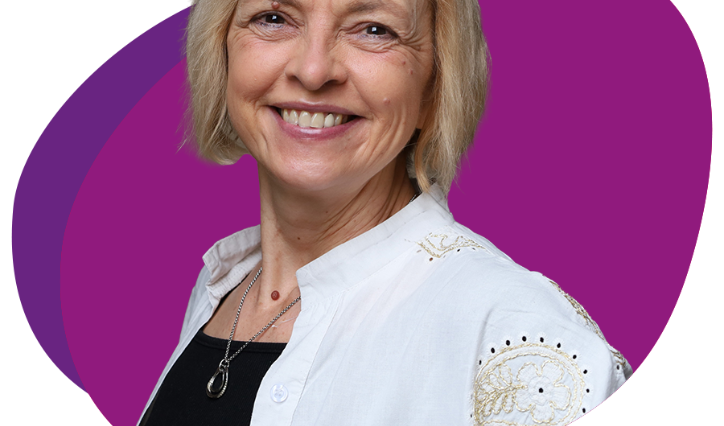 Freundlich lachende Frau mit kinnlangem, blondem Haar schaut in die Kamera.