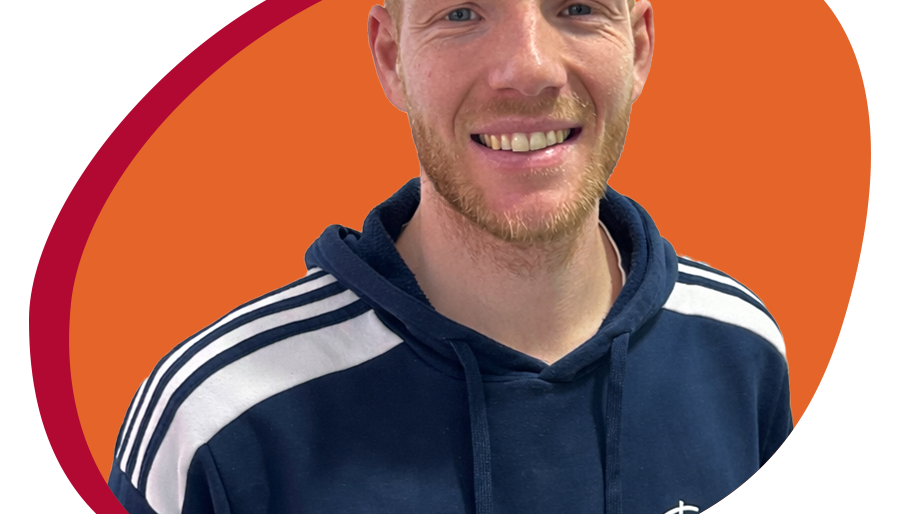 Junger Mann mit Trainingespulli lächelt freundlich in die Kamera.