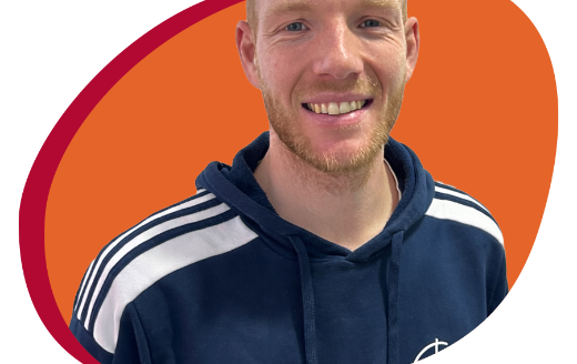 Junger Mann mit Trainingespulli lächelt freundlich in die Kamera.