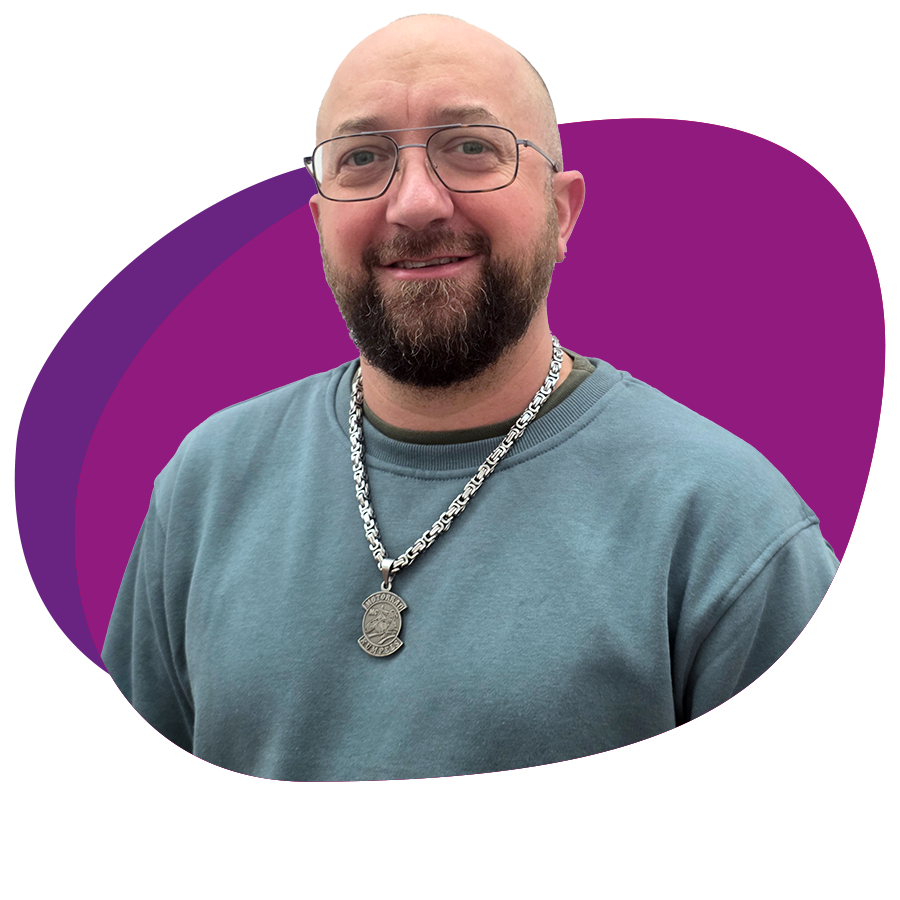 Mann mit Vollbart und Brille schaut freundlich in die Kamera. Er trägt eine auffällige Kette um den Hals.