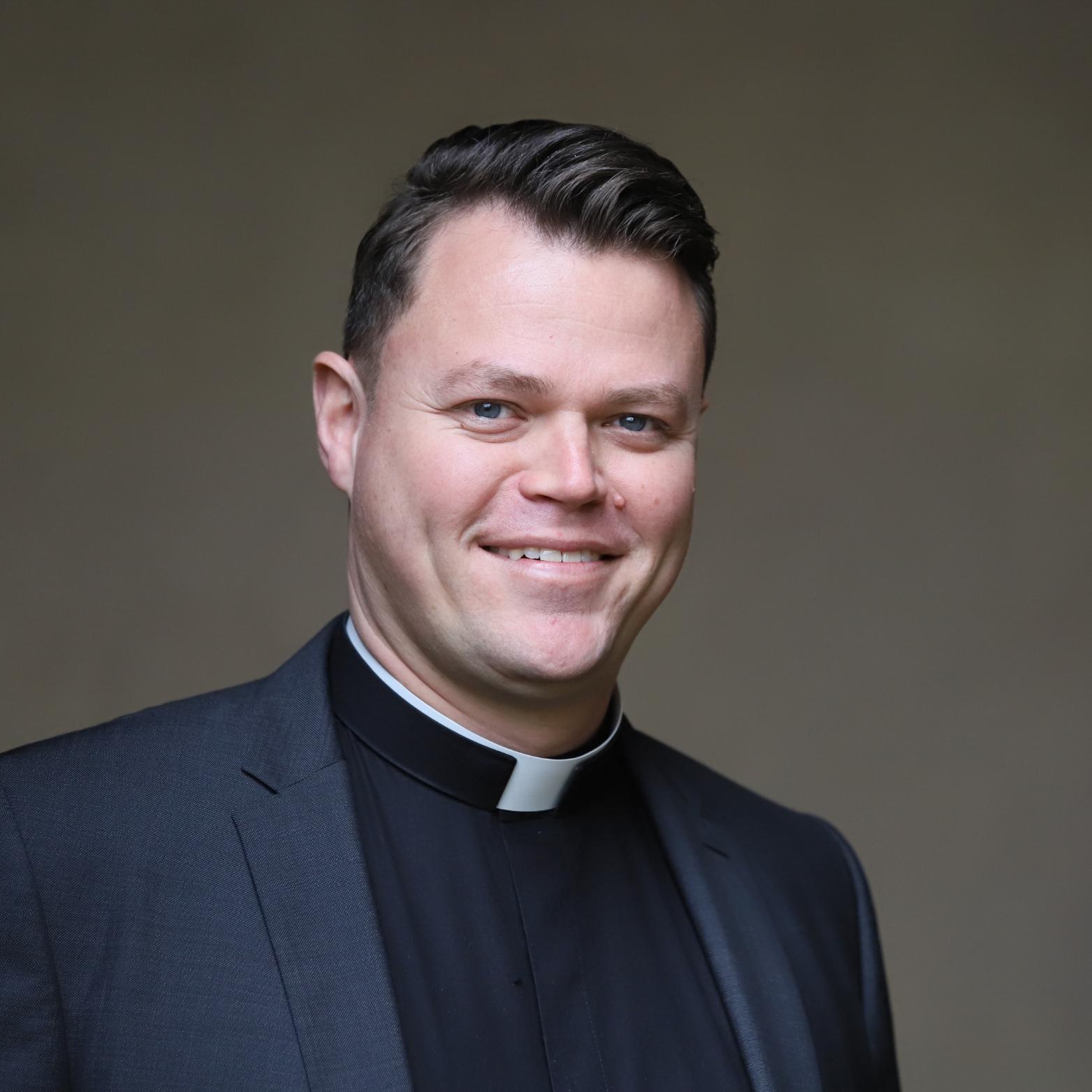 ein junger Priester vor einem grauen Hintergrund