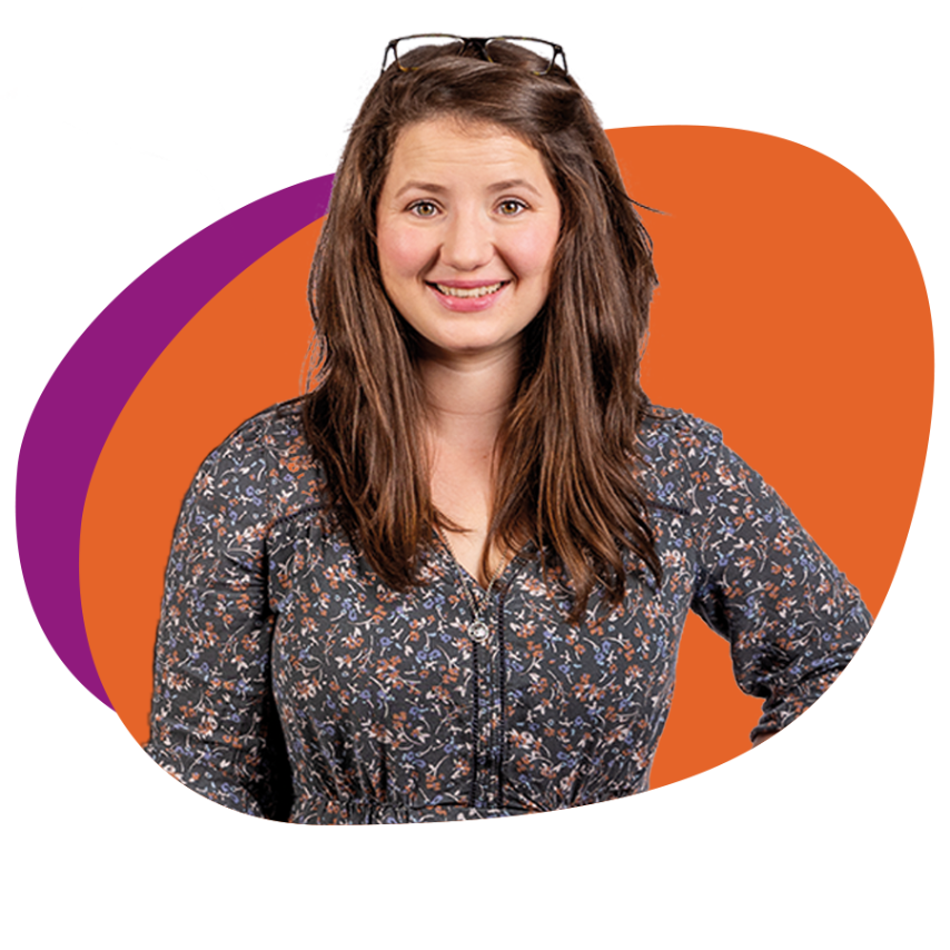 Junge Frau mit langen braunen Haaren und Blümchenkleid schaut lächelnd in die Kamera