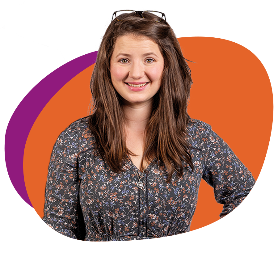 Junge Frau mit langen braunen Haaren und Blümchenkleid schaut lächelnd in die Kamera