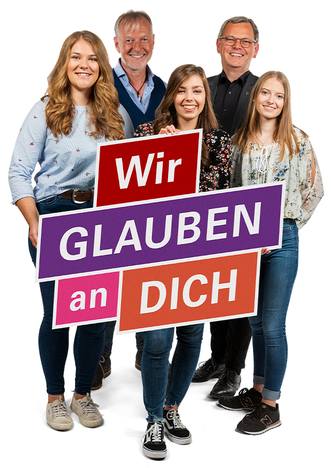Ein Gruppenfoto von 5 Personen, drei Frauen stehen im Vordergrund. Zwei Männer stehen in der hitneren Reihe. Die Person in der Mitte der vorderen Reihe hält ein Schild mit dem Text 'Wir glauben an dich' in der Hand