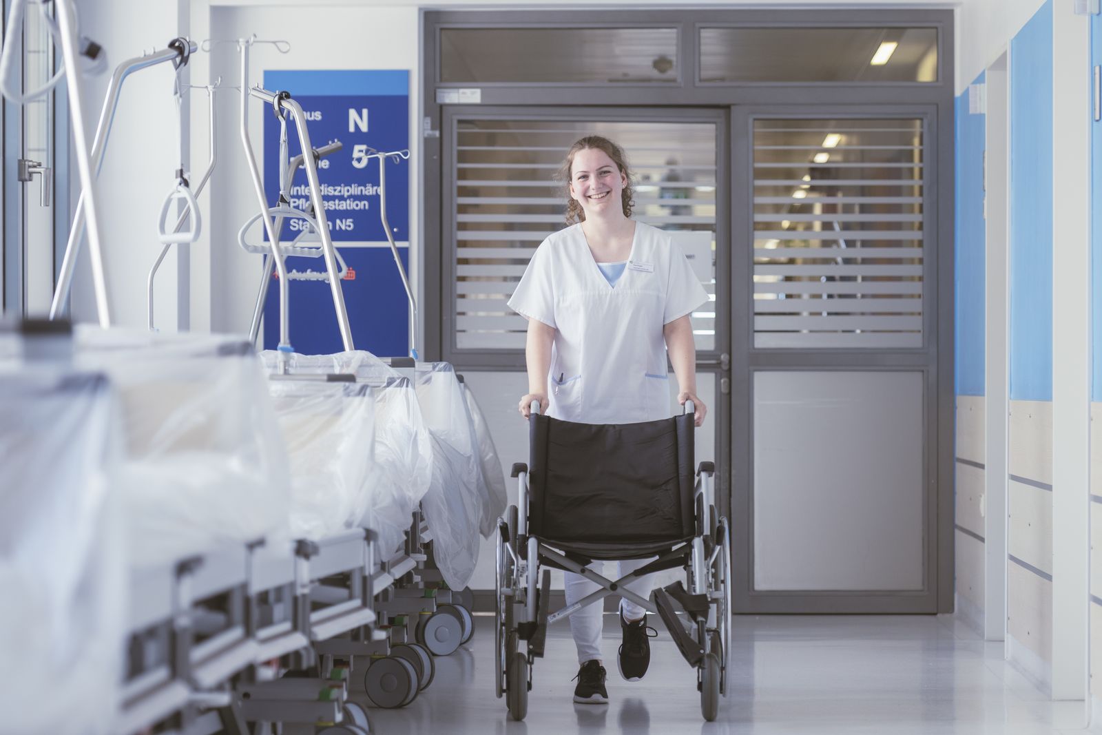 Eine Freiwillige schiebt einen leeren Rollstuhl durch den Krankenhausgang.