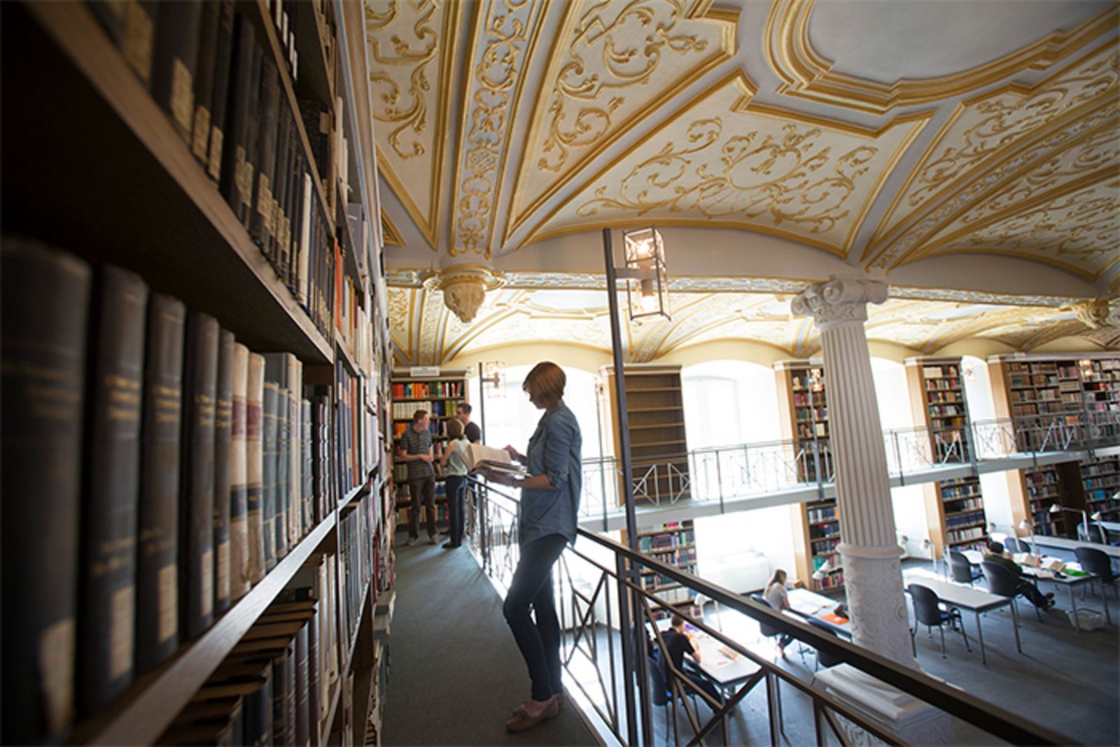 Ein Blick von oben in die Bibliothek des Priesterseminars mit dem beeindruckenden Deckengewölbe. Eine junge Frau blättert in einem Buch.