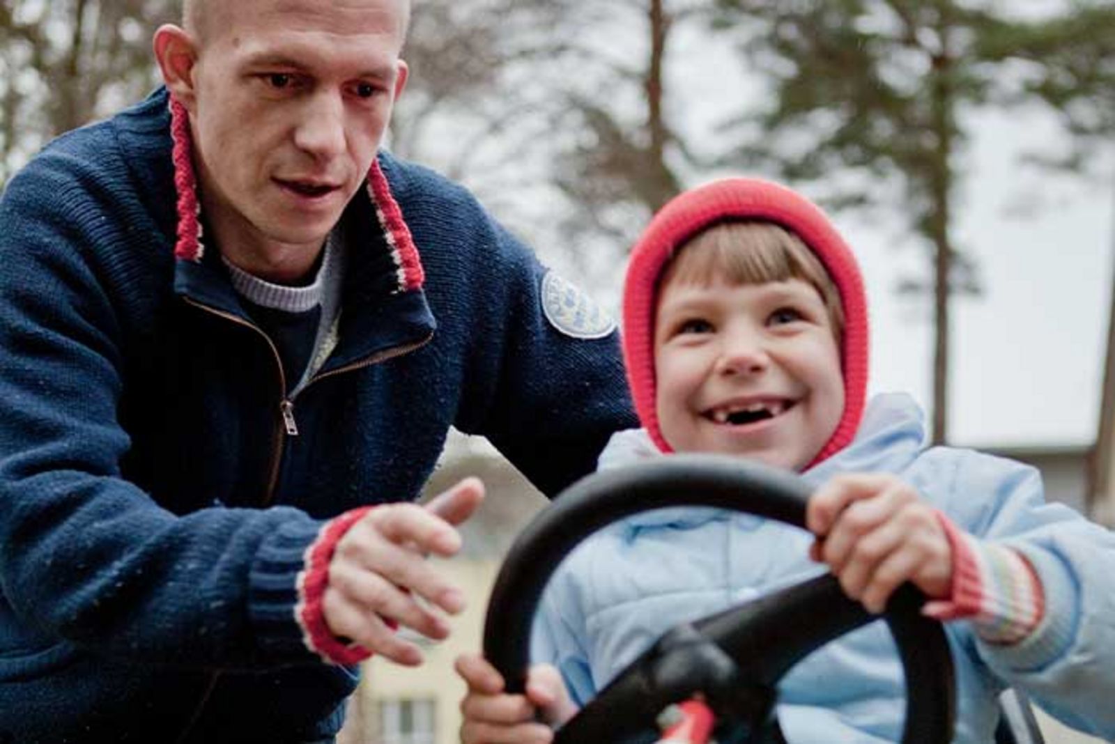ein mann spielt mit einem Kind draußen. Es sitzt auf einem Kinderfahrzeug und lacht fröhlich.