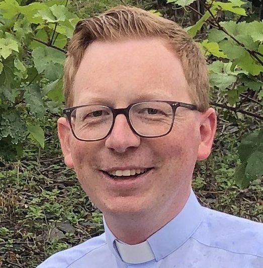 Junger Mann mit Brille und Collarhemd lächelt 