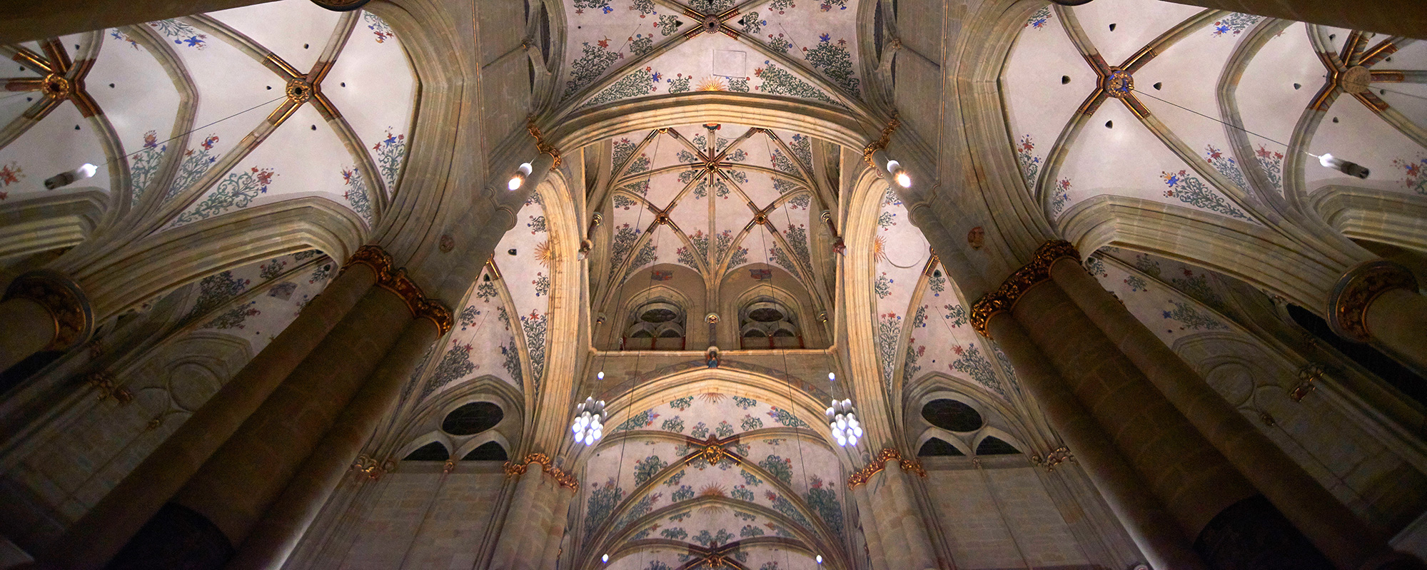 Ein hell erleuchtetes Deckengewölbe einer Kirche mit blauen Ornamenten und roten Ausläufern.